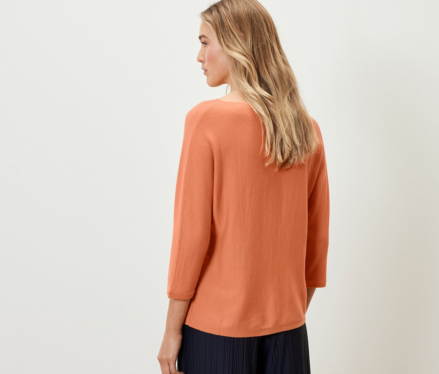Une femme, vue de dos, porte un pull en maille fine de laine mérinos pêche.