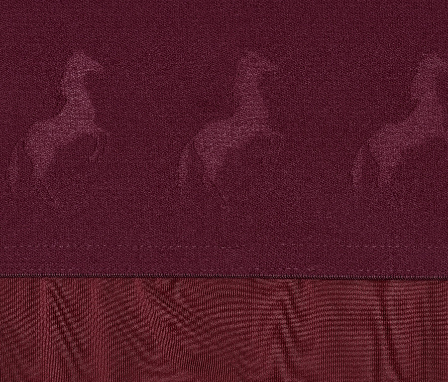 Gros plan sur un collant d'équitation rouge avec assise anti-dérapante intégrale pour enfant, orné de motifs de chevaux.