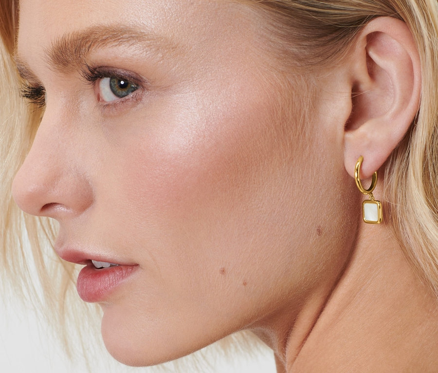 Profil d'une femme blonde avec les mains derrière la tête portant des créoles avec des pendentifs en nacre.