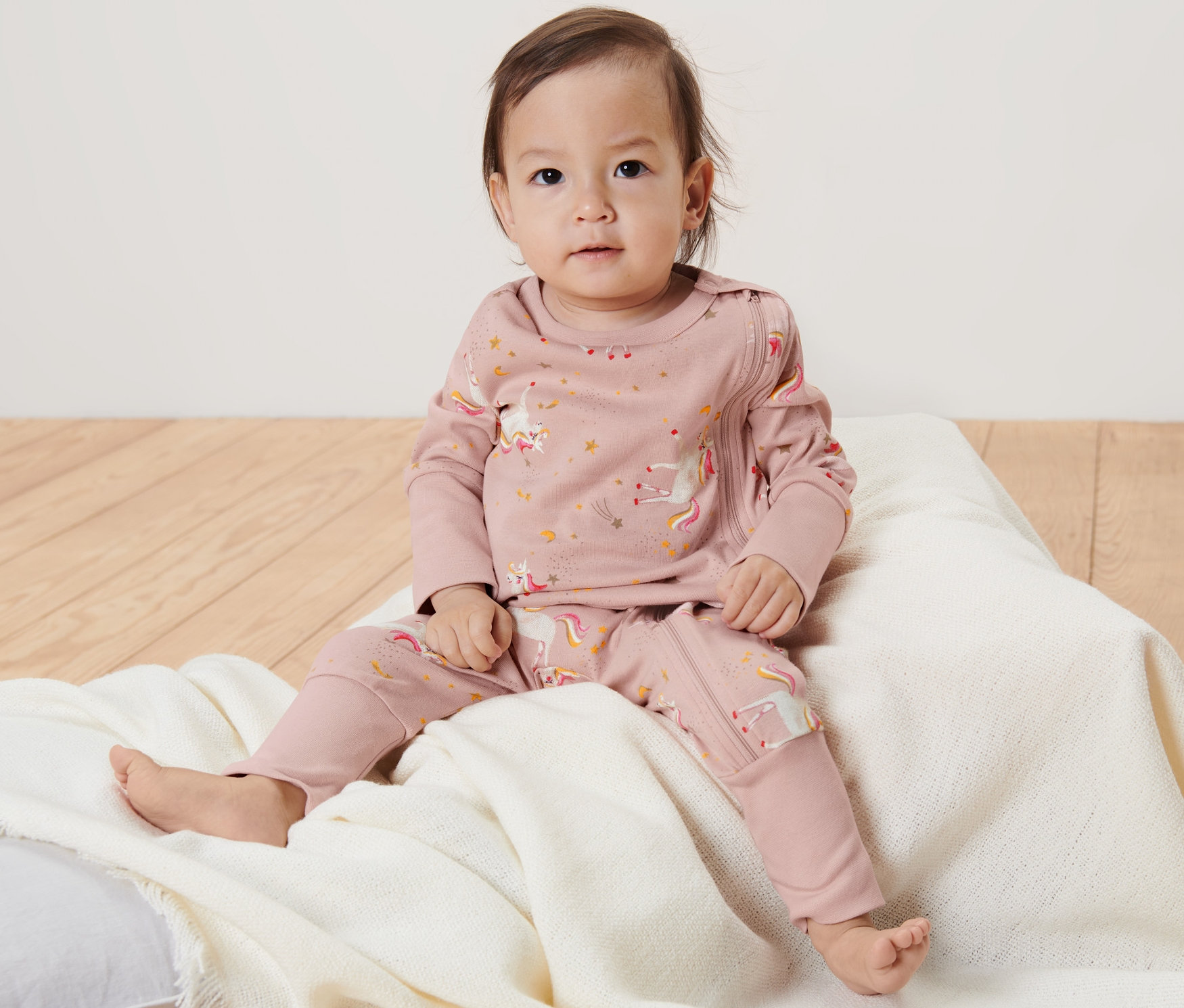 Un bébé est assis sur un coussin et porte un pyjama rose licorne.