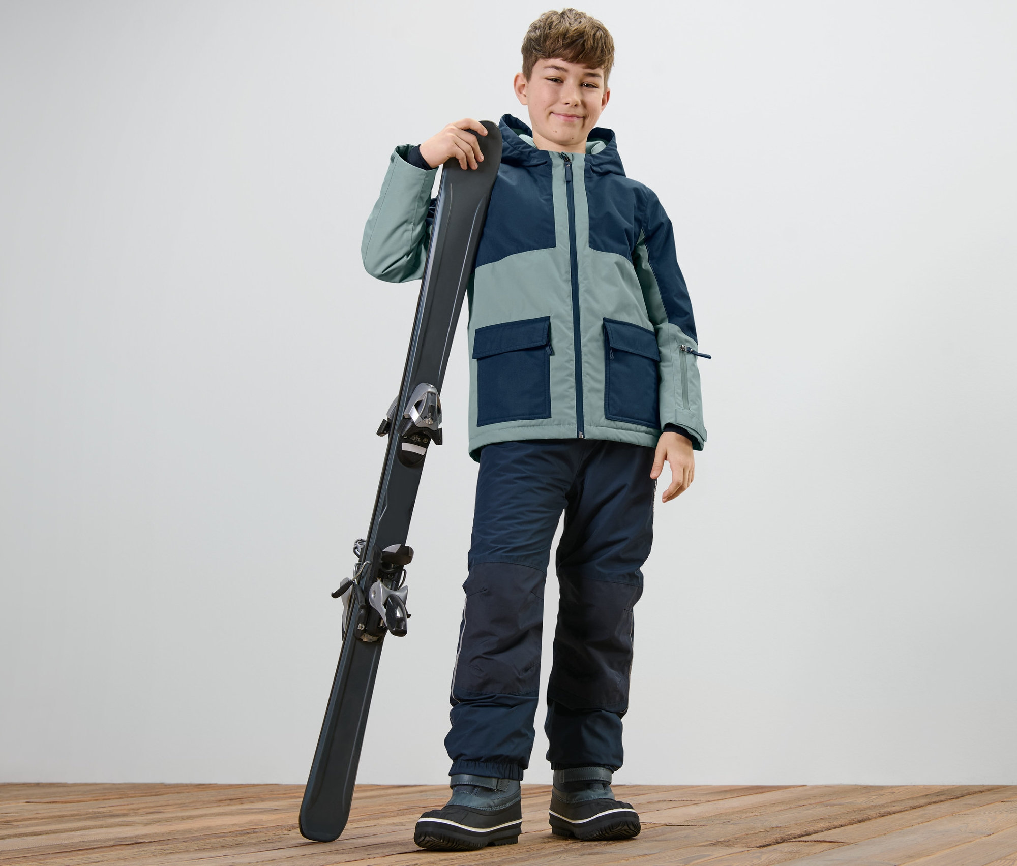 Garçon portant une veste de snowboard et de plein air pour enfant tenant des skis.