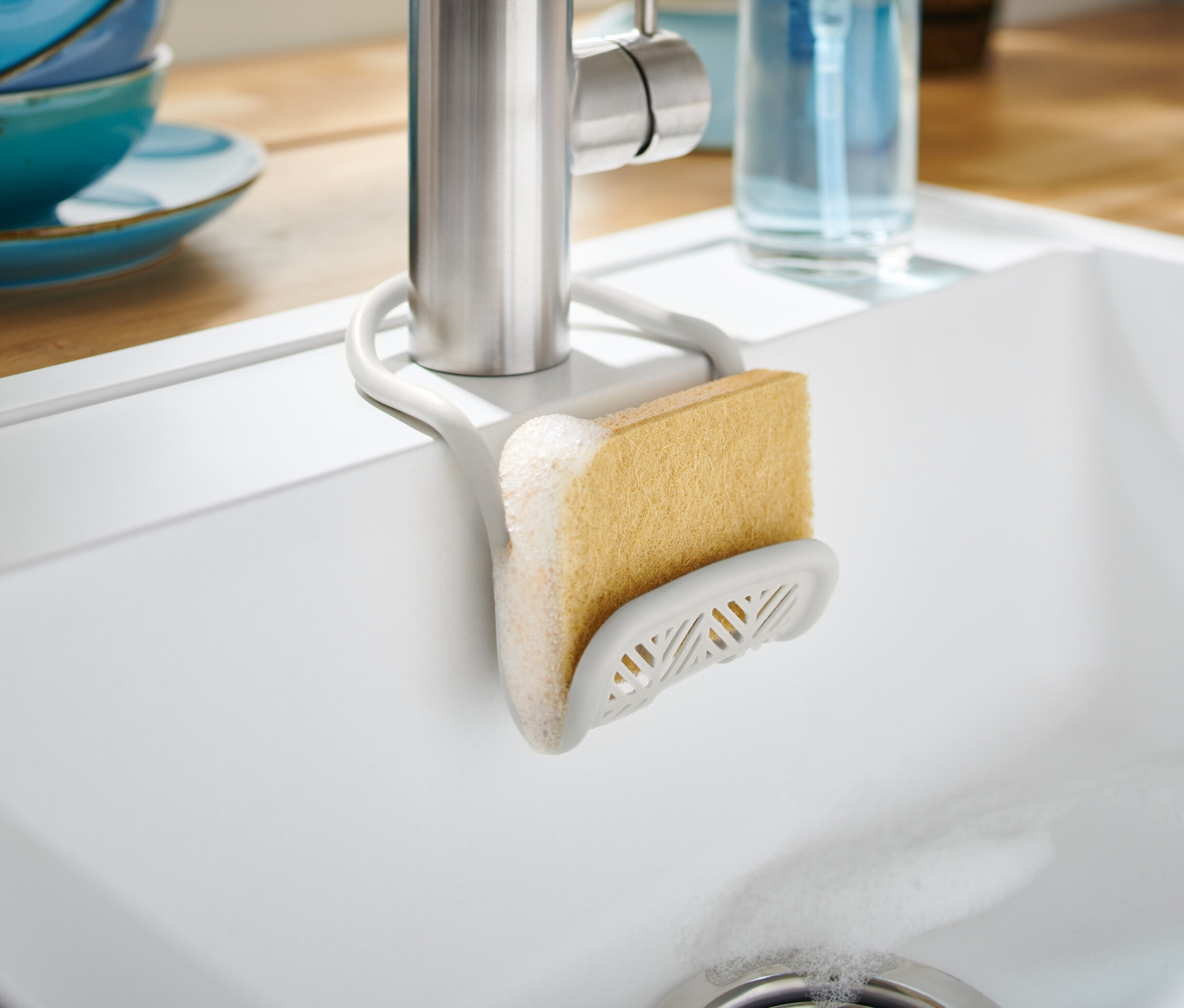 Porte-éponge avec éponge fixé sur un robinet dans un évier blanc.