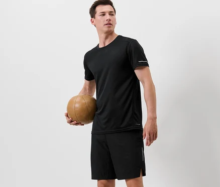 Un homme tient un ballon de basket et porte un t-shirt technique noir.
