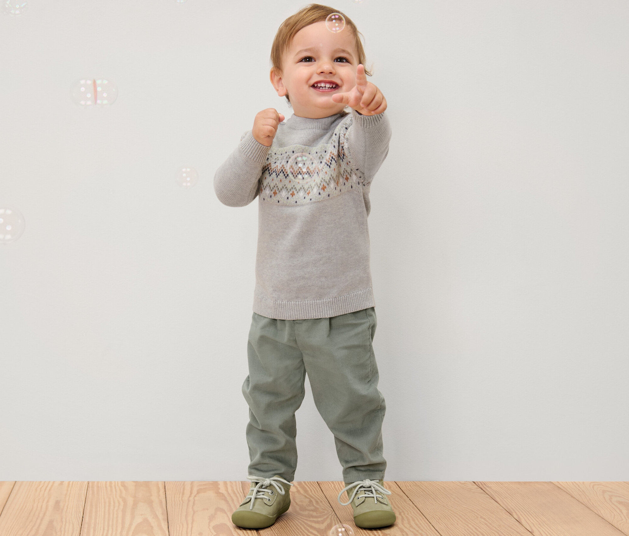 Un garçon pointe du doigt, portant un pull gris et un pantalon en velours à enfiler pour enfant.