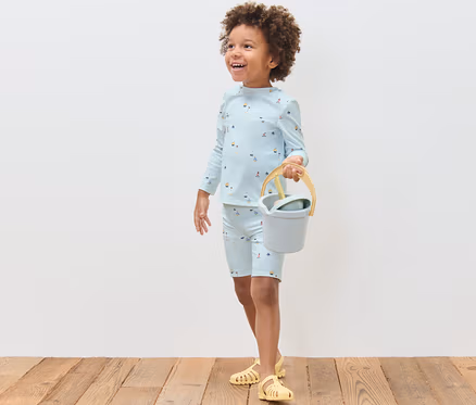 Garçon portant un ensemble pour enfant avec indice de protection UV 80, marin, tenant un seau et une pelle.