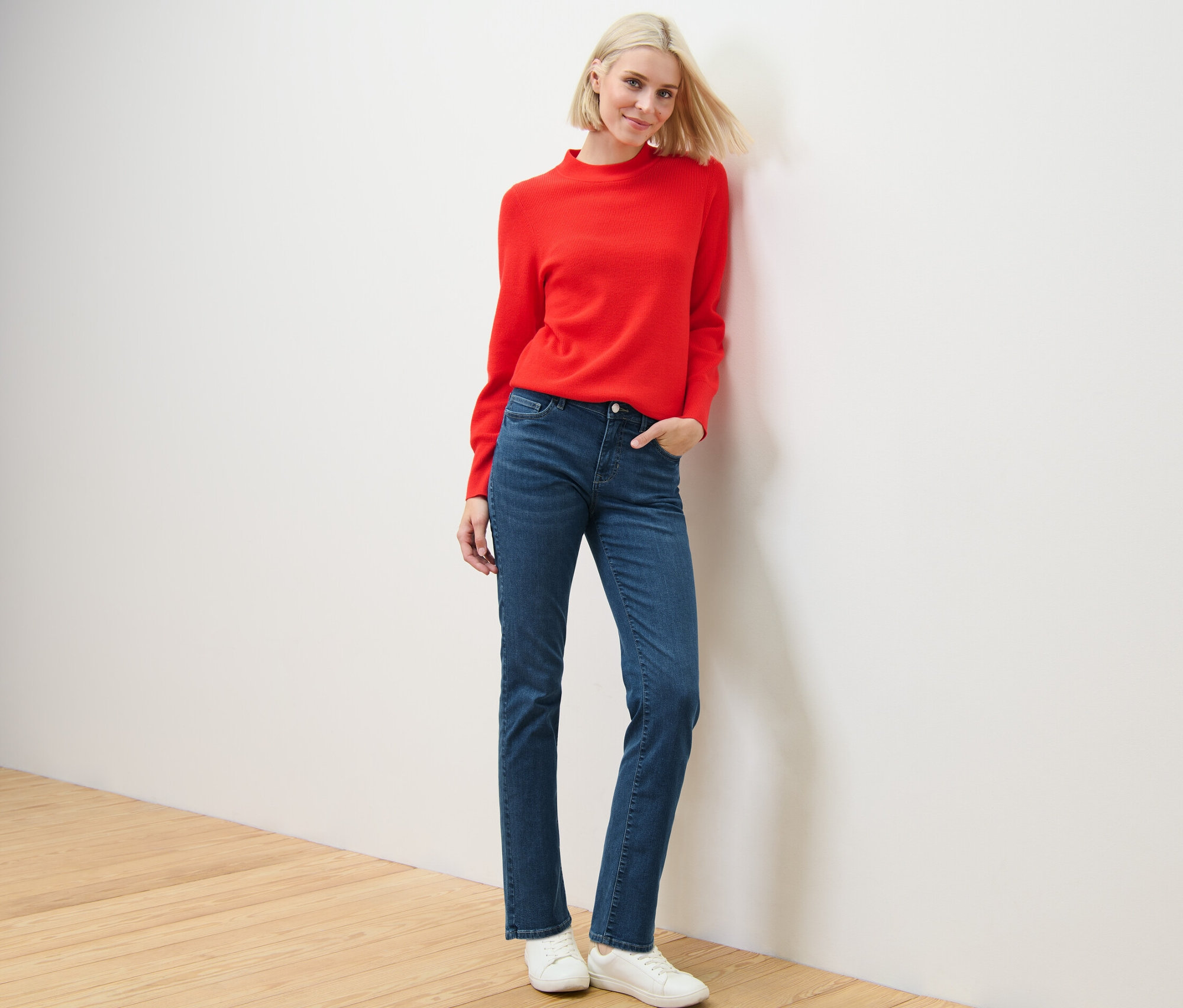 Une femme blonde pose en pull rouge et jean droit – Fit « Kira ».