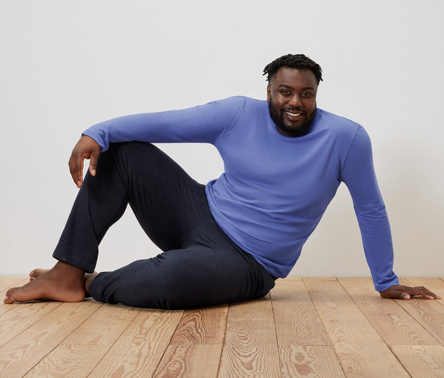 Un homme est assis sur un plancher en bois dans un pyjama bleu/bleu foncé.