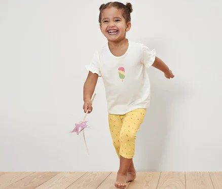 Fillette souriante posant dans un t-shirt avec un dessin de glace et un legging ¾ rose/jaune pour enfant.