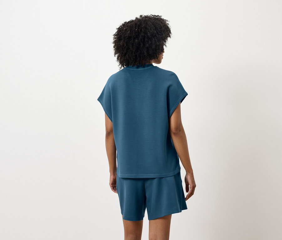 Une femme, vue de dos, porte un haut et un short bleu-vert.
