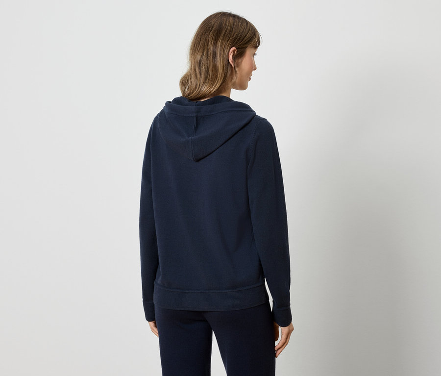Une femme, vue de dos, porte un sweat à capuche bleu marine et un pantalon de survêtement.