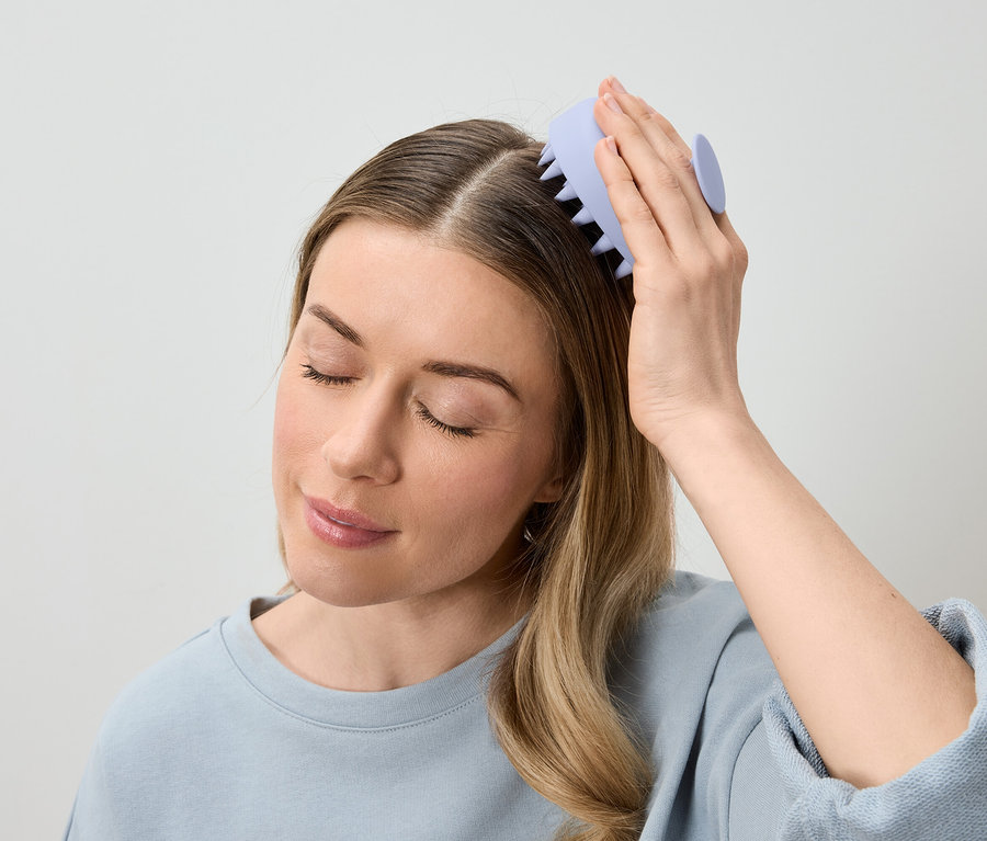 Une femme se masse le cuir chevelu avec une brosse de massage capillaire violet clair.