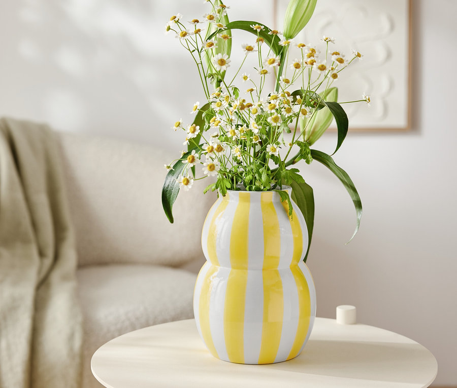 Fleurs dans un vase rayé jaune et blanc sur une petite table ronde. Fauteuil et décorations en arrière-plan.