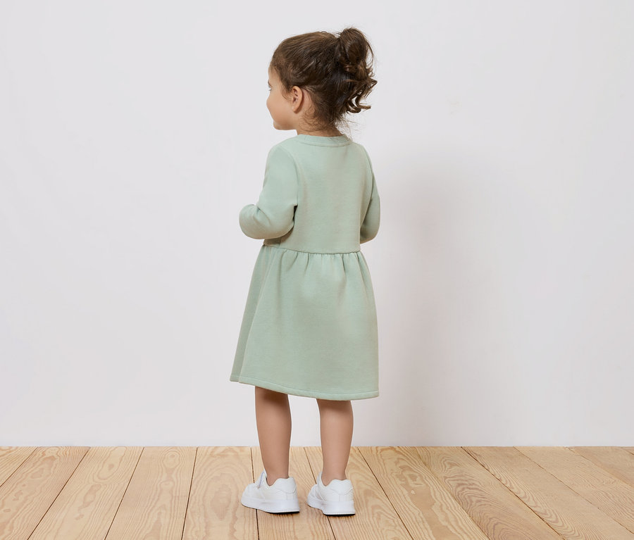 Fillette en robe verte et chaussures blanches, vue de dos.