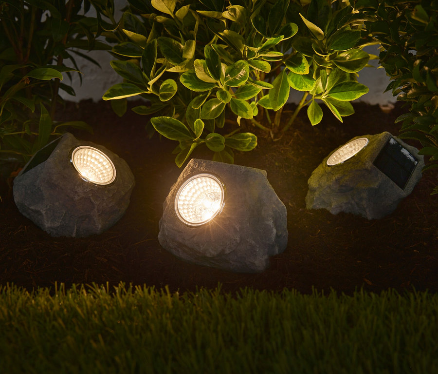 Trois pierres à LED solaires Premium illuminent un parterre de fleurs.