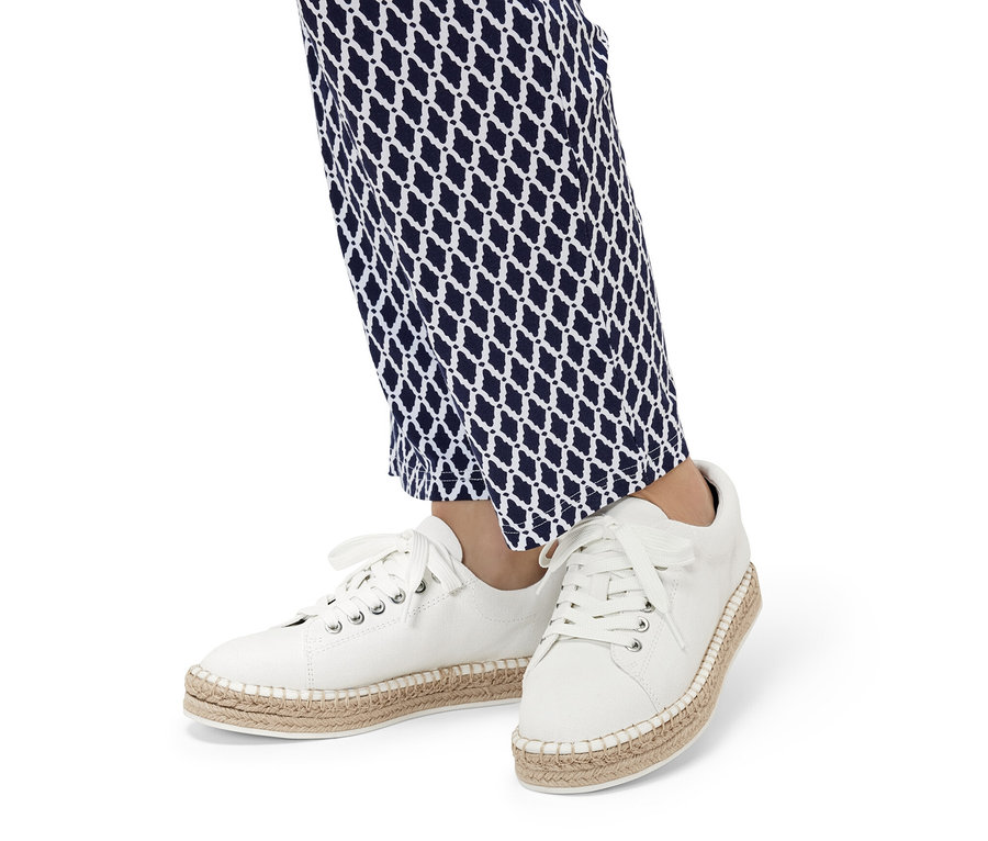 Jambes portant un pantalon à motifs bleu et blanc et des baskets en toile blanches.