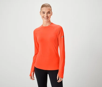 Une femme souriante portant un t-shirt orange à manches longues et un legging noir.