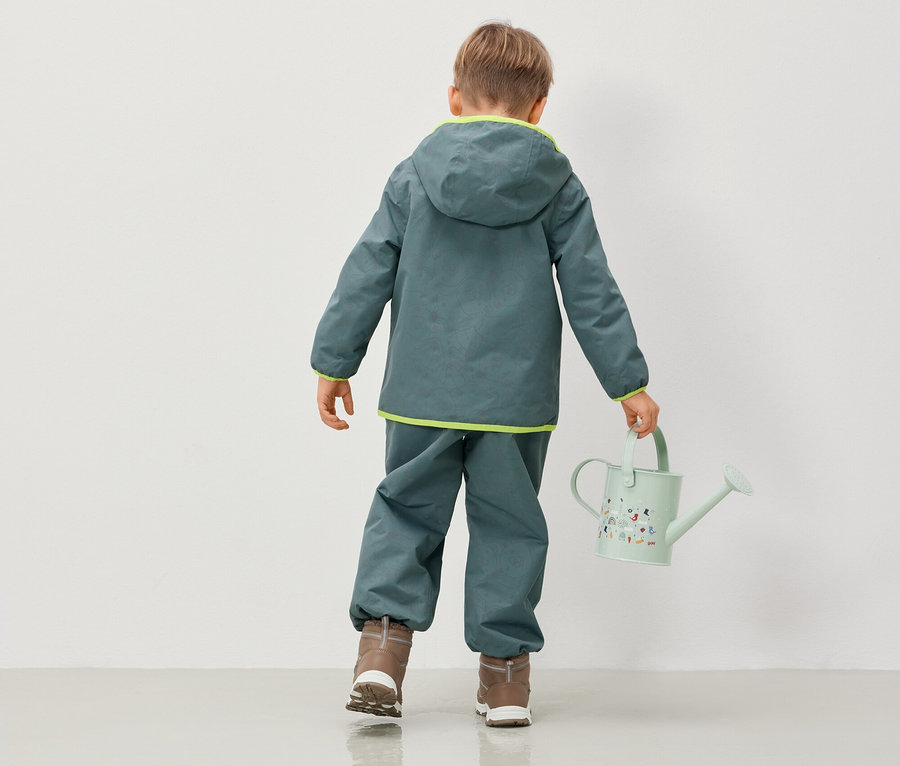 Garçon en veste à capuche et pantalon tenant un arrosoir.