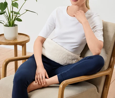 Une femme assise dans un fauteuil avec un coussin chauffant sur le ventre.