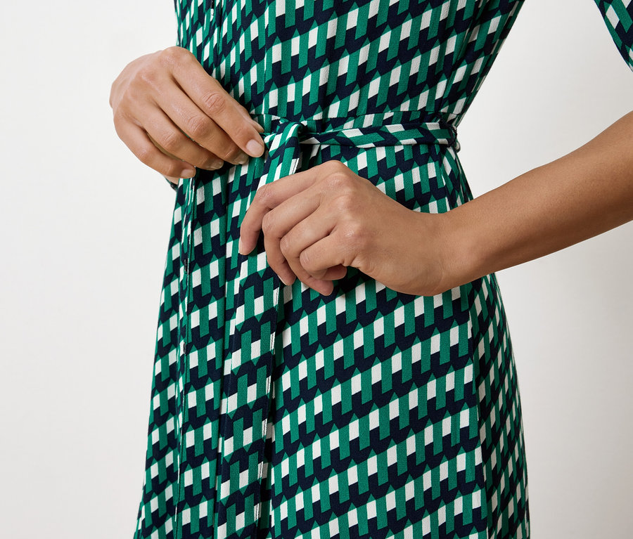 Femme nouant la ceinture d'une robe verte, blanche et bleu marine.