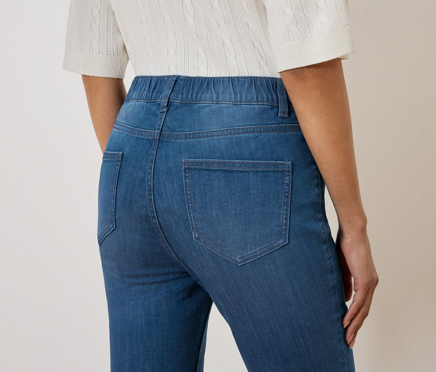 Gros plan sur le dos d'une femme portant un jean bleu à taille élastique et un chemisier tricoté blanc.