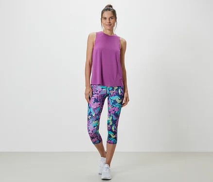 Une femme portant un débardeur de sport turquoise d'un ensemble deux pièces et un legging à motifs floraux.