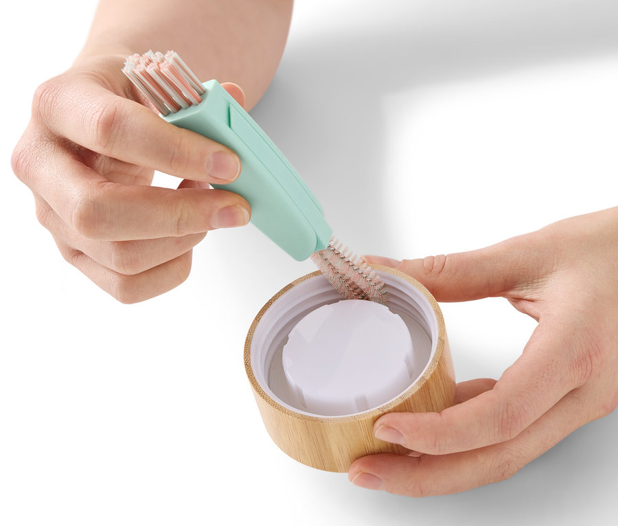 Une femme nettoie un couvercle de bouteille avec une brosse de nettoyage 3 en 1.