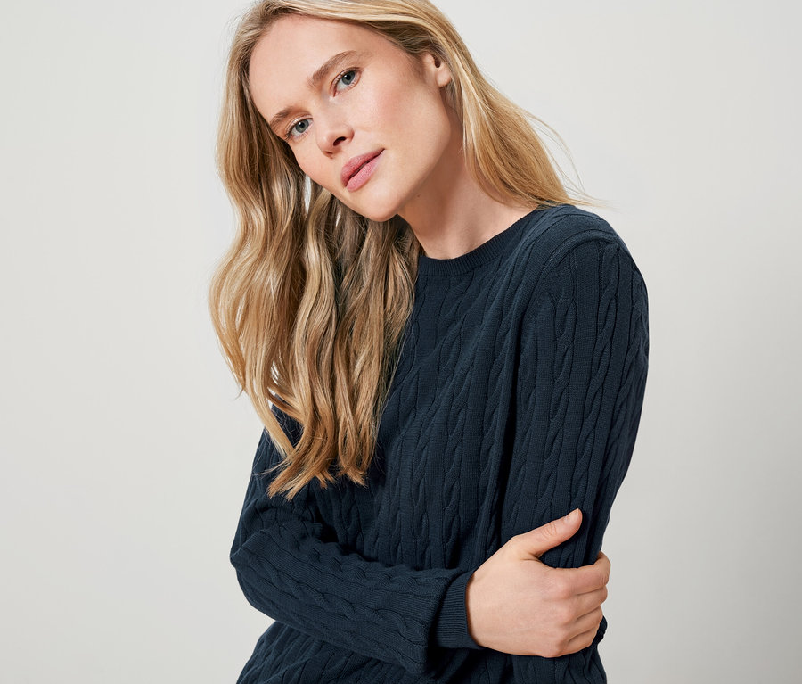 Une femme blonde porte un pull en maille bleu foncé.