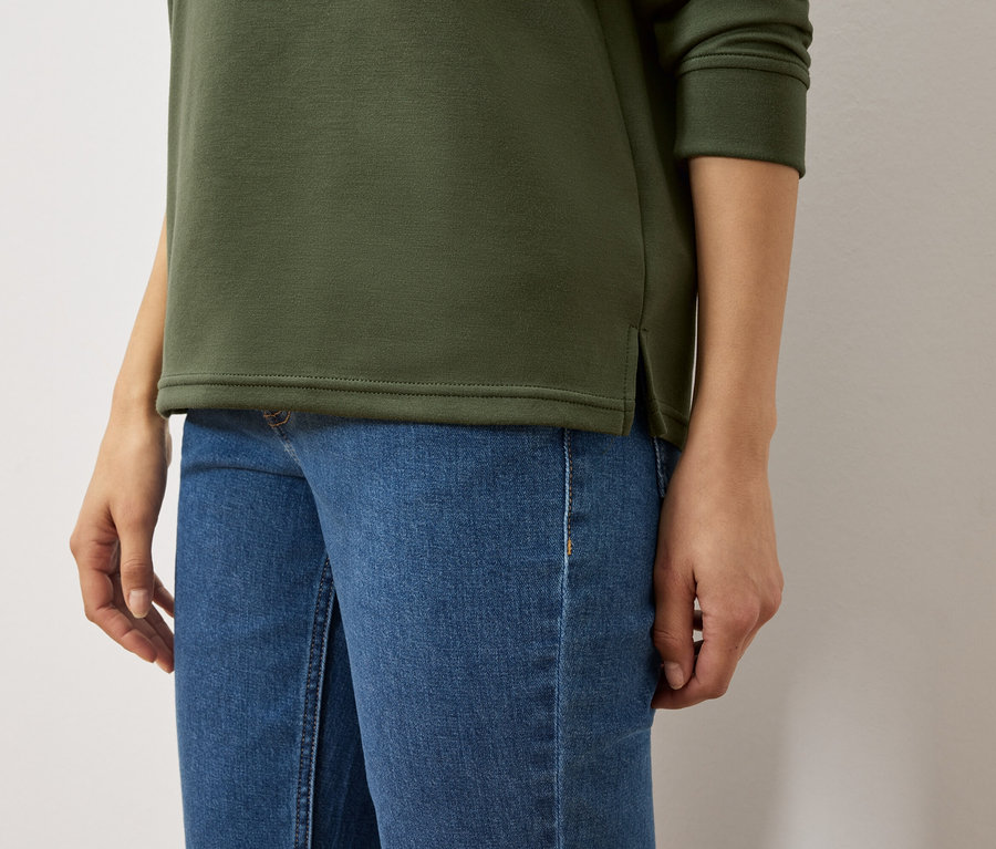 Torse d'une femme portant un sweat-shirt vert olive et un jean bleu.