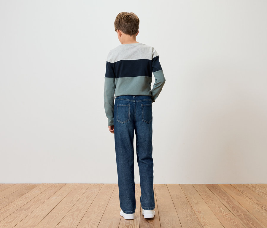 Un garçon se tient dos à la caméra, portant un pull rayé et un jean bleu.