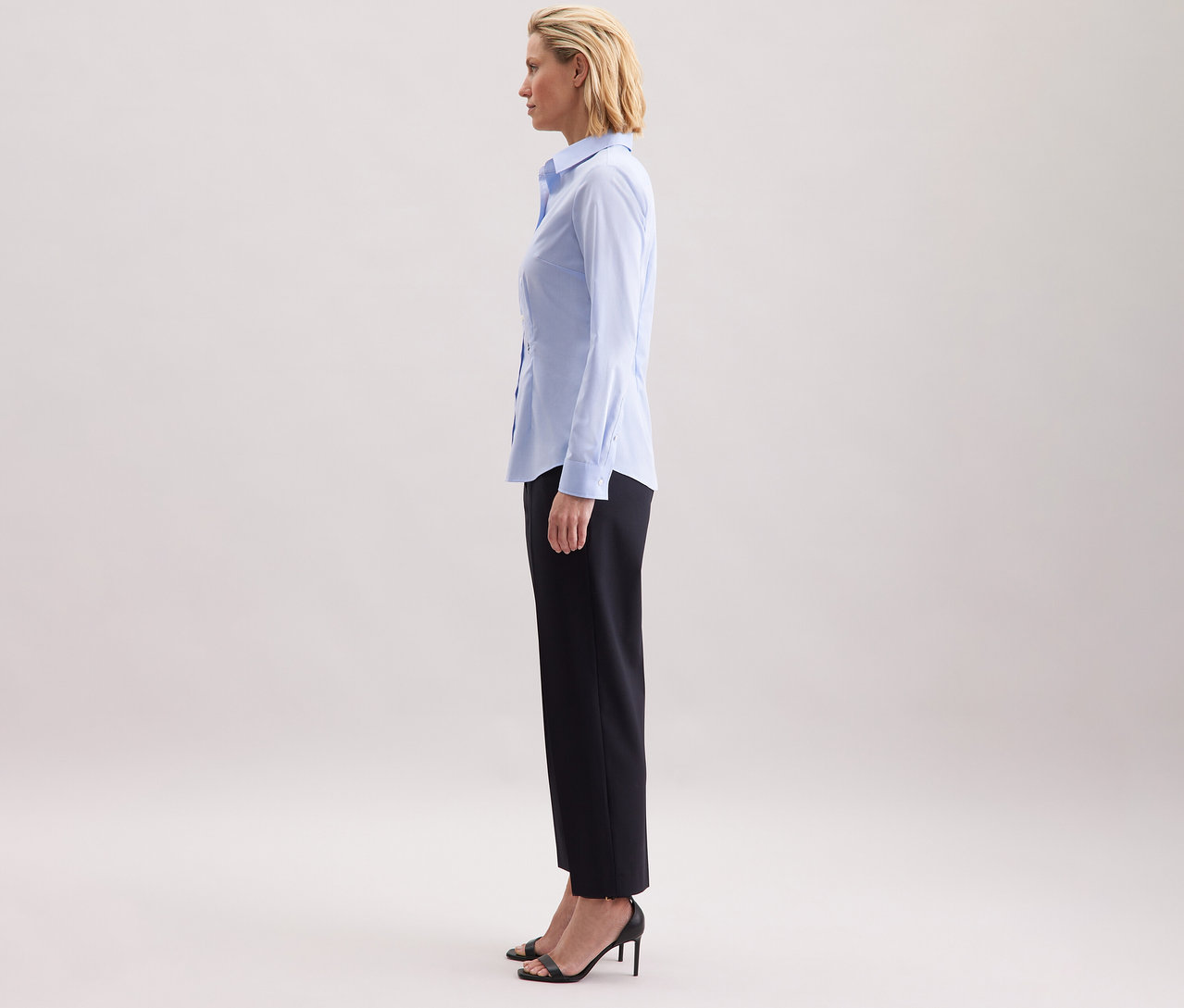 Femme debout de profil portant un chemisier bleu clair Slim Fit non iron Seidensticker.