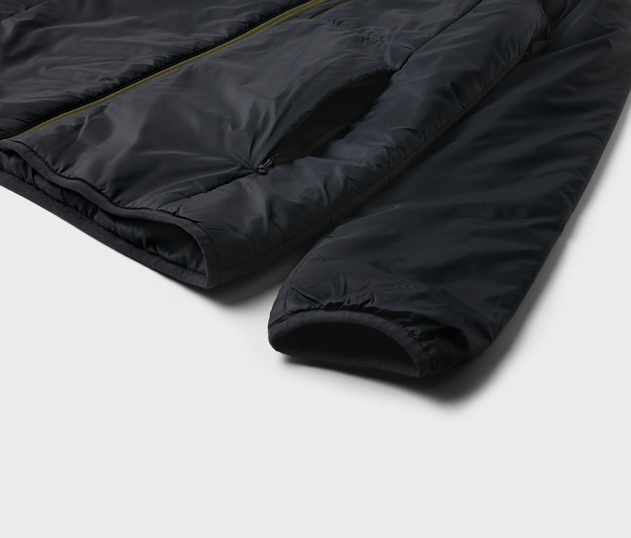 Gros plan d'une veste noire avec une poche et une manche sur un fond clair.