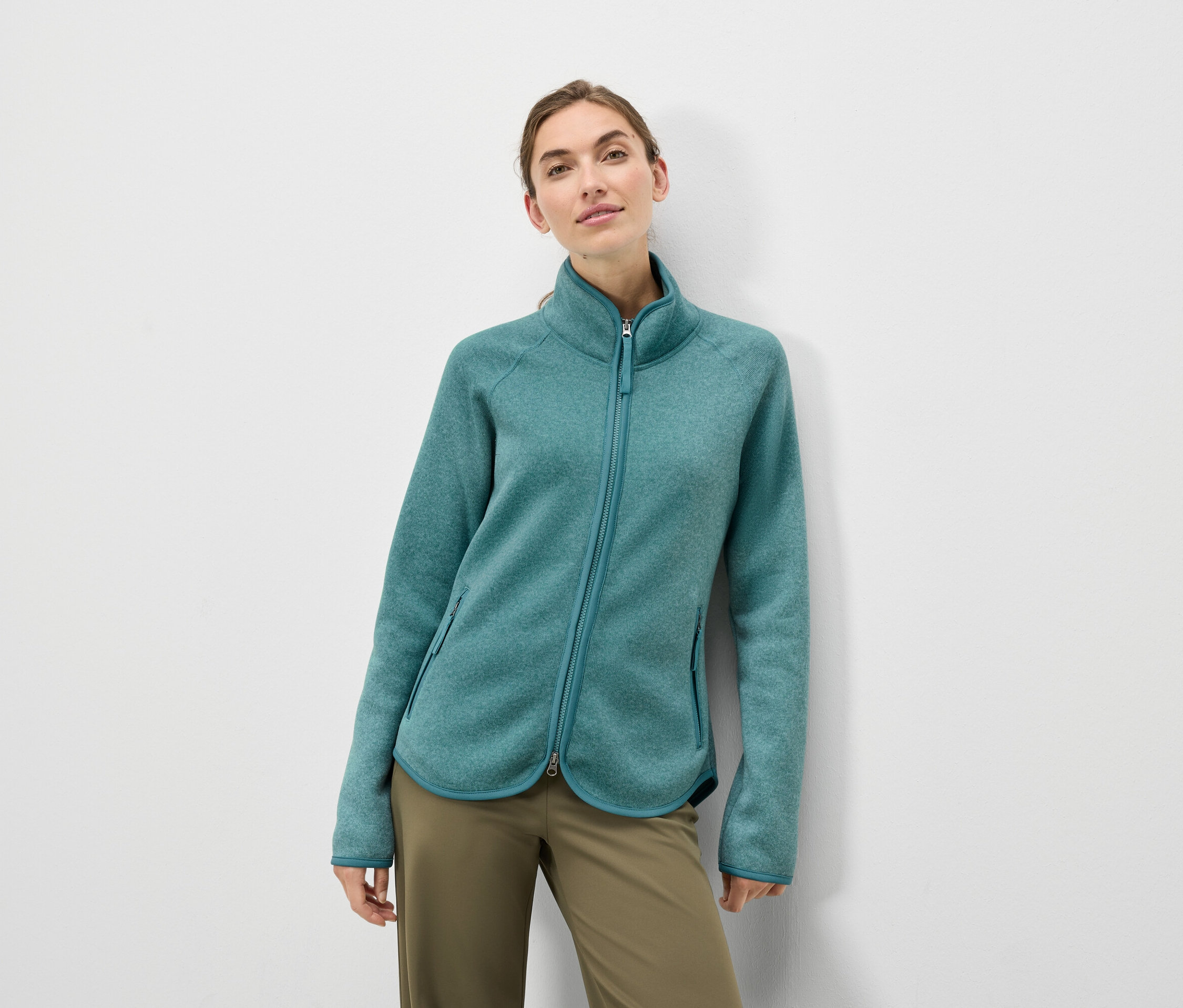 Une femme porte une veste en polaire turquoise et un pantalon vert olive.
