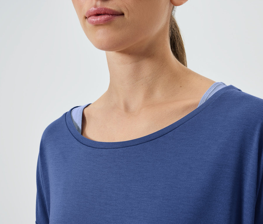 Gros plan d'une femme aux cheveux bruns portant un t-shirt bleu à manches courtes et un débardeur bleu.