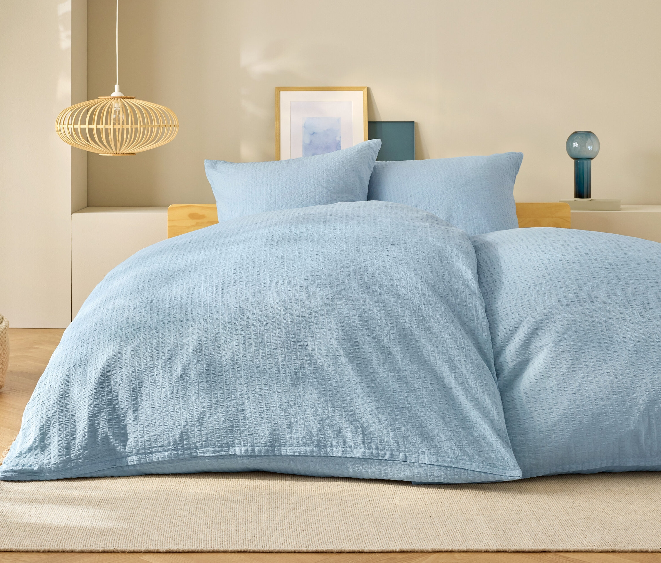 Linge de lit bleu clair sur un lit avec des oreillers et une lampe en arrière-plan.