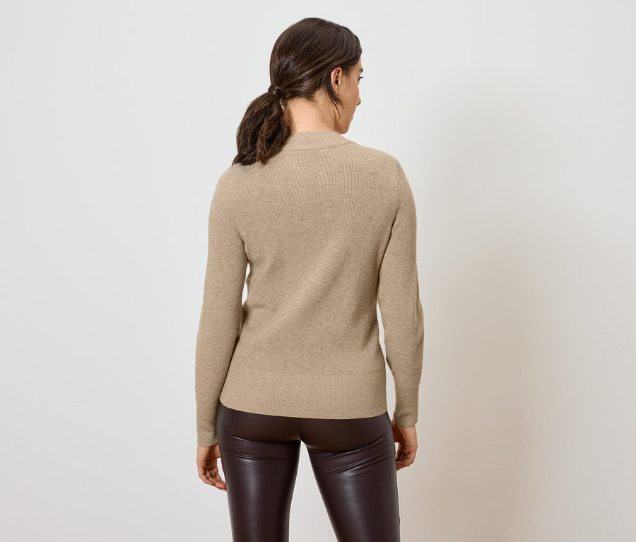 Une femme, dos à la caméra, porte un pull beige et un pantalon en cuir marron.