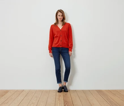 Une femme se tient debout et porte un cardigan orange, un jean et des mocassins noirs.