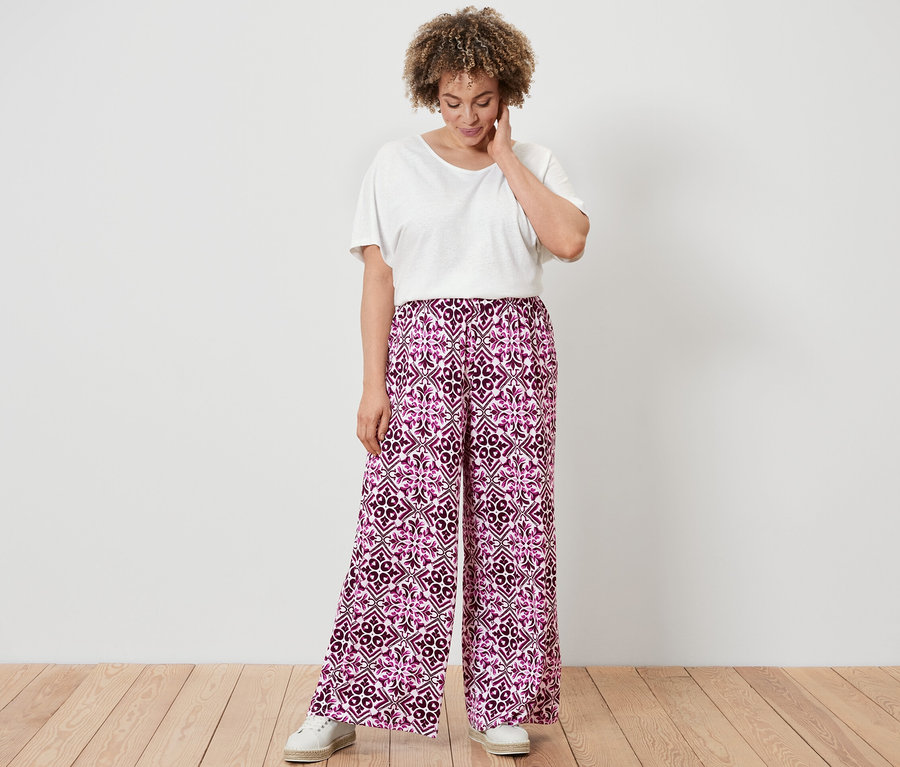 Une femme portant un T-shirt blanc en lin mélangé et un pantalon palazzo imprimé baies se tient sur un plancher en bois.