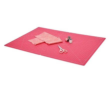 Des ciseaux, du tissu et trois bobines de fil reposent sur un tapis de découpe et de bricolage rose pliable.