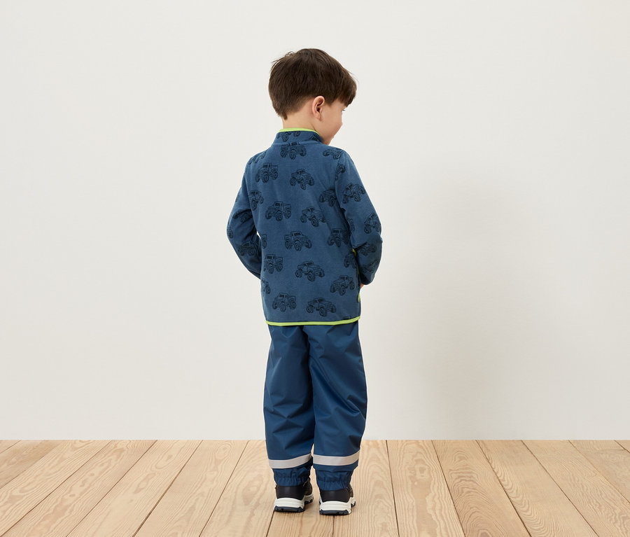 Un garçon, vu de dos, porte un ensemble bleu avec des motifs de voitures.