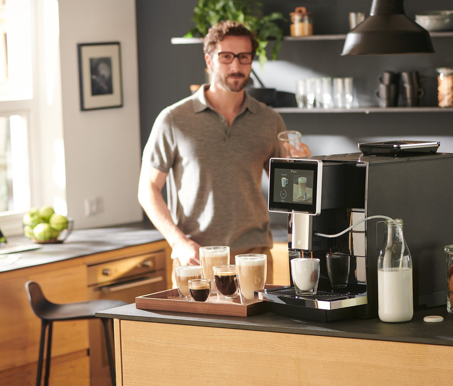 Un homme tient une tasse près d'une machine à café »Tchibo Office«, noire.