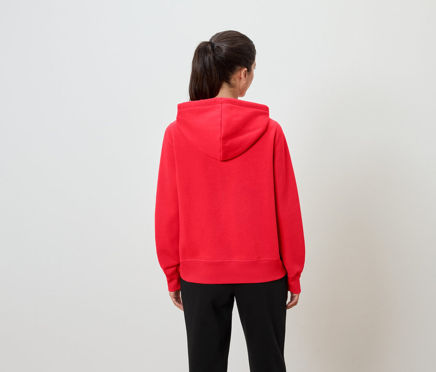 Une femme, de dos, porte un sweat à capuche rouge et un pantalon noir.