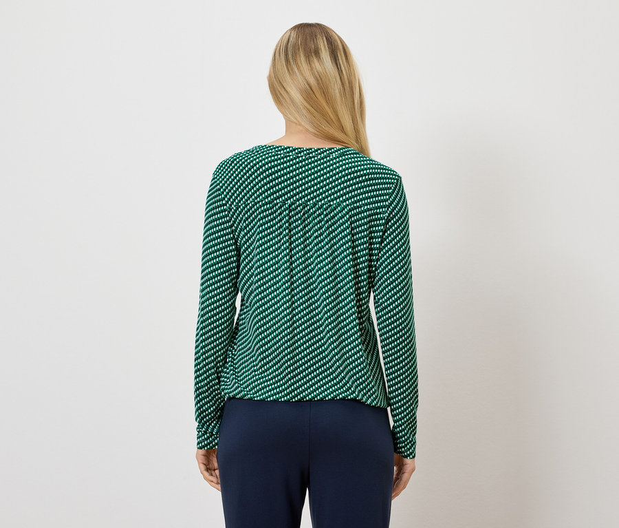 Une femme porte un haut à rayures vertes à manches longues et un pantalon bleu marine.