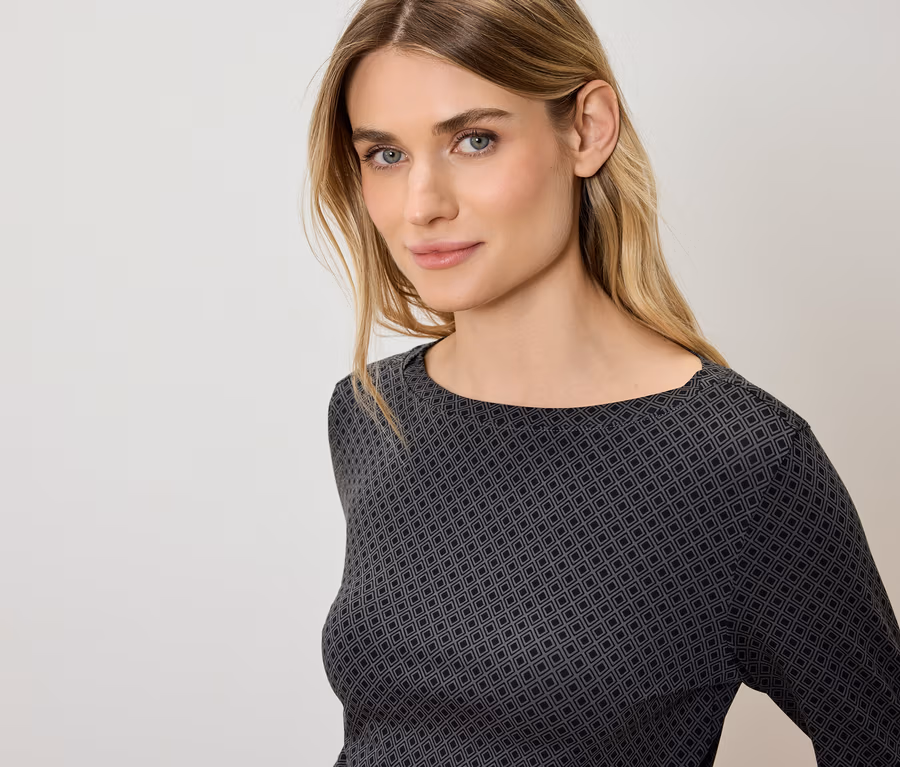 Portrait d'une femme blonde aux yeux bleus portant un haut gris et noir à motifs géométriques.