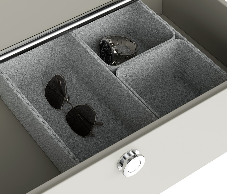 Dans un tiroir ouvert, des lunettes de soleil et une montre argentée reposent dans des coupelles en feutre gris.