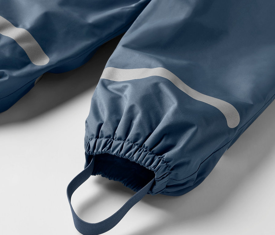Gros plan sur un pantalon de pluie thermique bleu pour enfant, avec des réflecteurs et des ourlets élastiques.