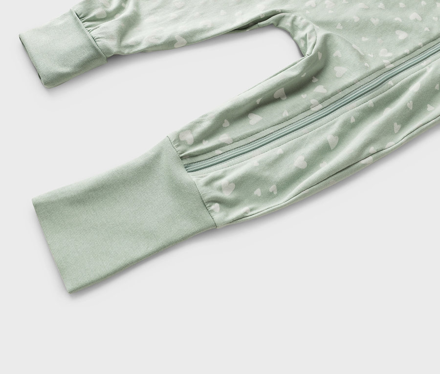 Gros plan d'un pyjama de bébé vert clair avec un motif de cœur blanc et une fermeture éclair.