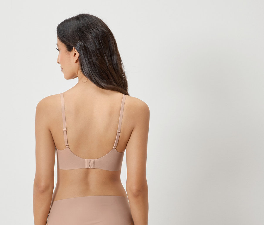 Vue arrière d'une femme aux cheveux foncés portant un soutien-gorge couleur chair et une culotte assortie.