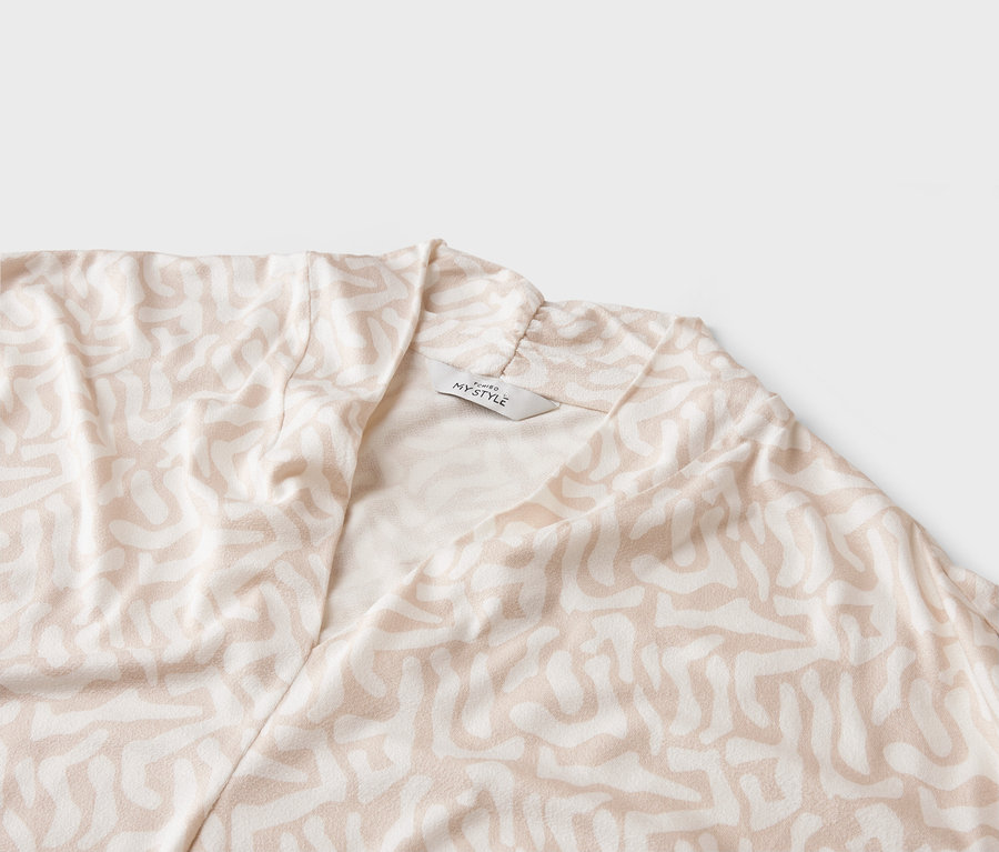 Gros plan d'un manteau clair avec un motif abstrait et une étiquette 'MY STYLE'.