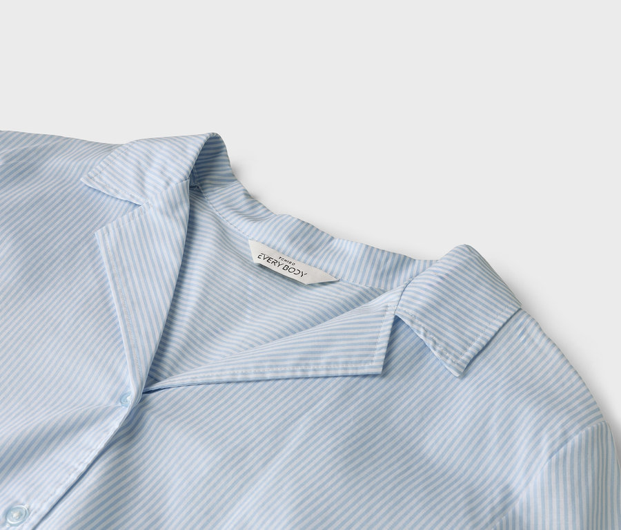 Gros plan d'une chemise rayée bleu clair avec un col et une étiquette « EVERYBODY » sur le col.