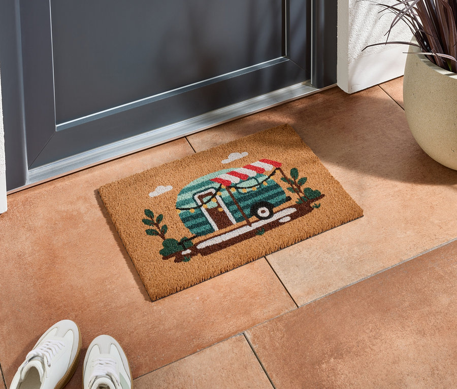 Un paillasson avec un motif de caravane se trouve devant une porte grise sur des carreaux de terre cuite.